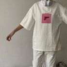 Weißes Oversize-T-Shirt mit rosa Pistolen-Print, kombiniert mit weißen Kopfhörern. Trendige Streetwear-Mode für Damen.