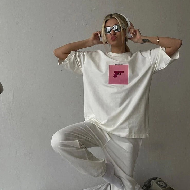 Frau in weißem Oversize-T-Shirt mit pinkem Print, Sonnenbrille und Kopfhörern. Trendige Streetwear, lässiger Look, modisches Statement.