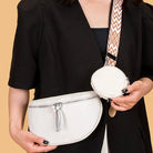 Frau mit weißer Leder-Gürteltasche und rundem Mini-Tasche, geometrischer Schulterriemen.
