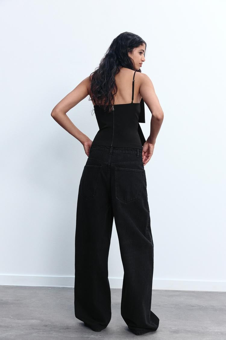 Frau in schwarzem Top und weiten Jeans, Rückansicht. Modetrend, lässiger Stil, Damenbekleidung, Streetwear, zeitgenössische Mode.