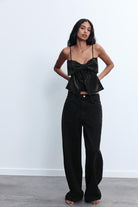 Frau in schwarzem, glitzerndem Top mit Schleife und weiten Jeans. Modetrend, eleganter Look, Damenmode, stilvolle Outfits, Freizeitkleidung.
