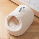 Kuscheliges, cremefarbenes Katzenbett aus Plüsch, rund, mit Griff, auf Holzboden.