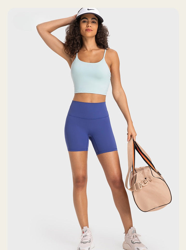 Frau in Sportbekleidung mit hellblauem Top und blauen Shorts, trägt weiße Sneaker und eine beige Sporttasche, ideal für Fitness und Yoga.