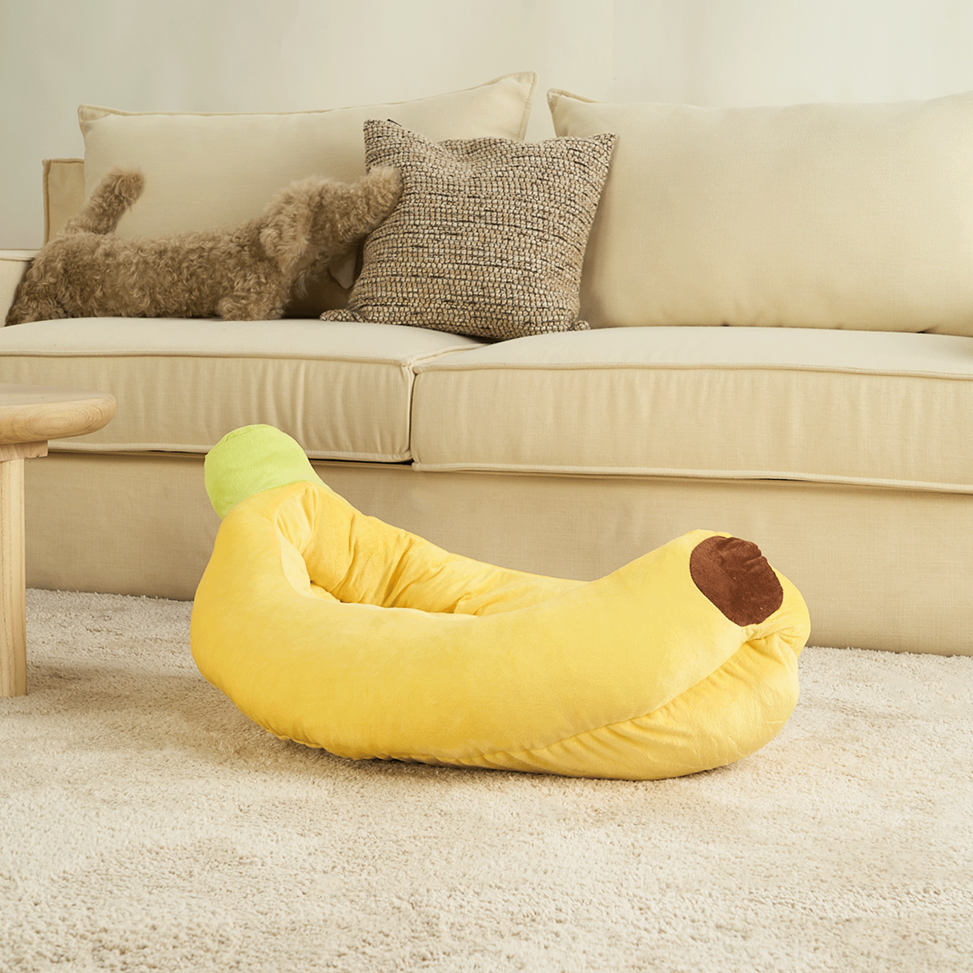 Gelbes Bananen-Sofa-Haustierbett auf beigem Teppich vor cremefarbenem Sofa.