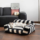 Gestreiftes Katzenbett aus Kunstlammwolle, breiter Armlehne, schwarz-weiß, auf Holzboden.