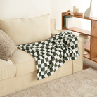 Schwarz-weiß karierte Flanell-Haustierdecke auf beigem Sofa im Wohnzimmer.