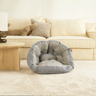 Graues Haustierbett aus Stoff vor beigem Sofa im Wohnzimmer.