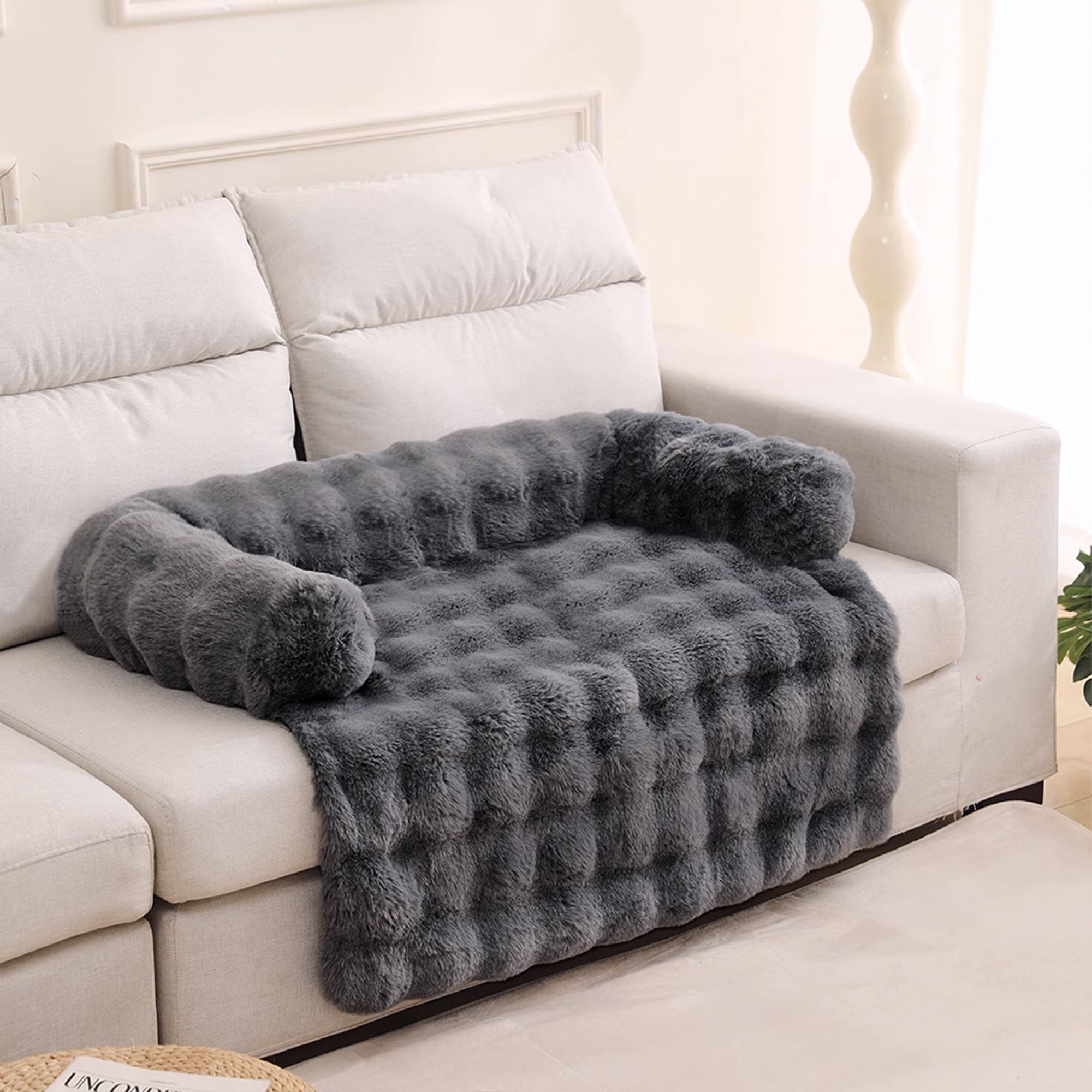 Graues, flauschiges Haustierbett auf weißem Sofa, gemütlich, weich, ideal für Hunde und Katzen.