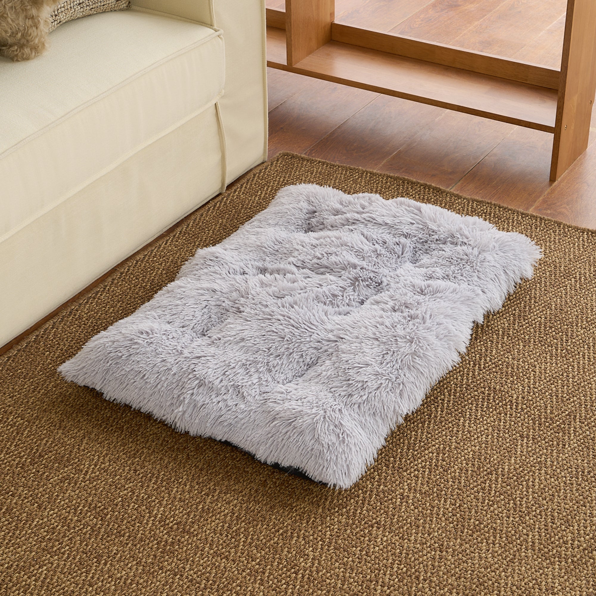 Graues, flauschiges Haustierbett auf Teppichboden neben Sofa, ideal für Hunde und Katzen.