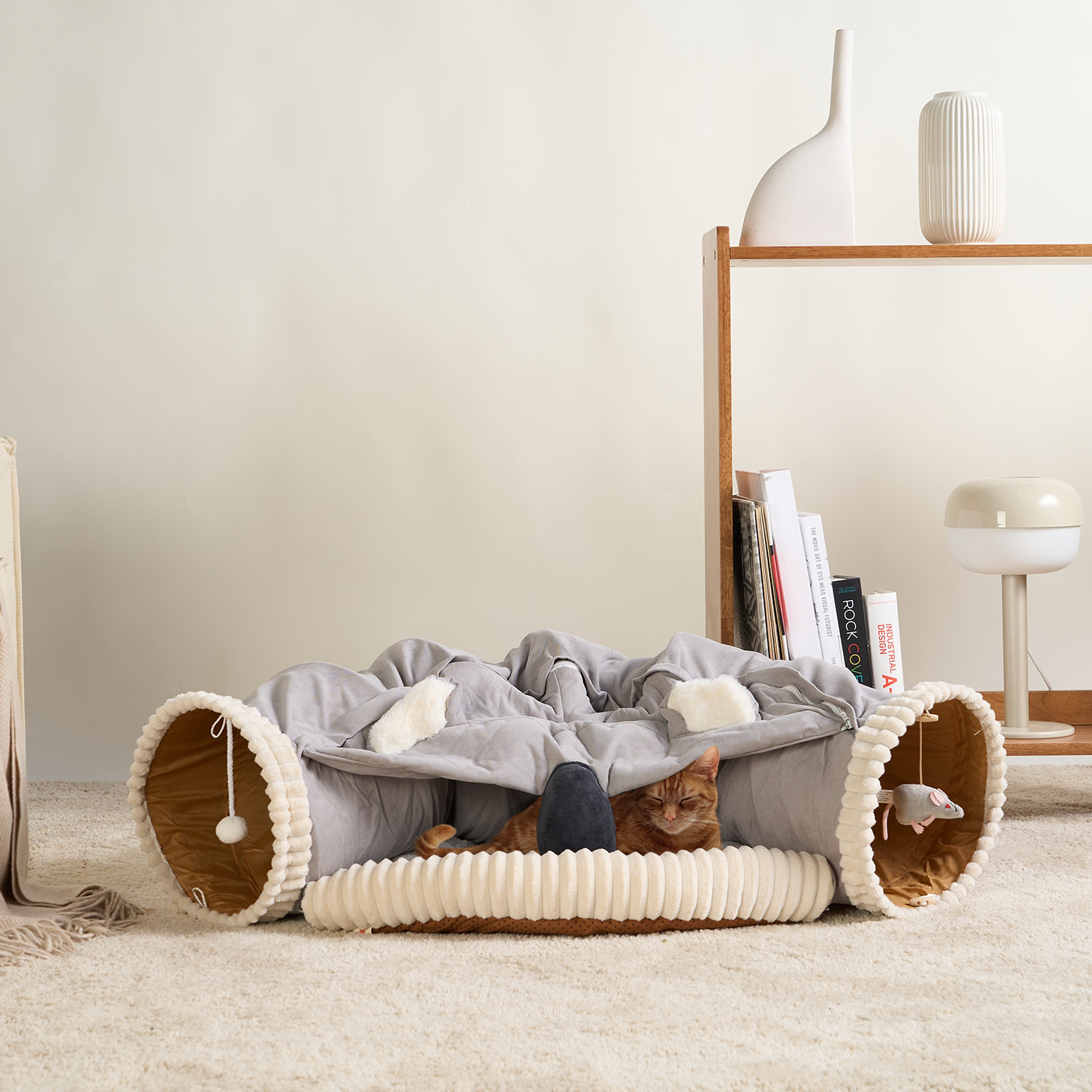 Graues 2-in-1-Katzenbett aus Stoff, Tunnel-Design, gemütlich, mit Spielzeug, auf Teppich.