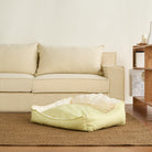 Gelbes Haustierbett aus Baumwolle auf Teppich vor beigem Sofa im Wohnzimmer.