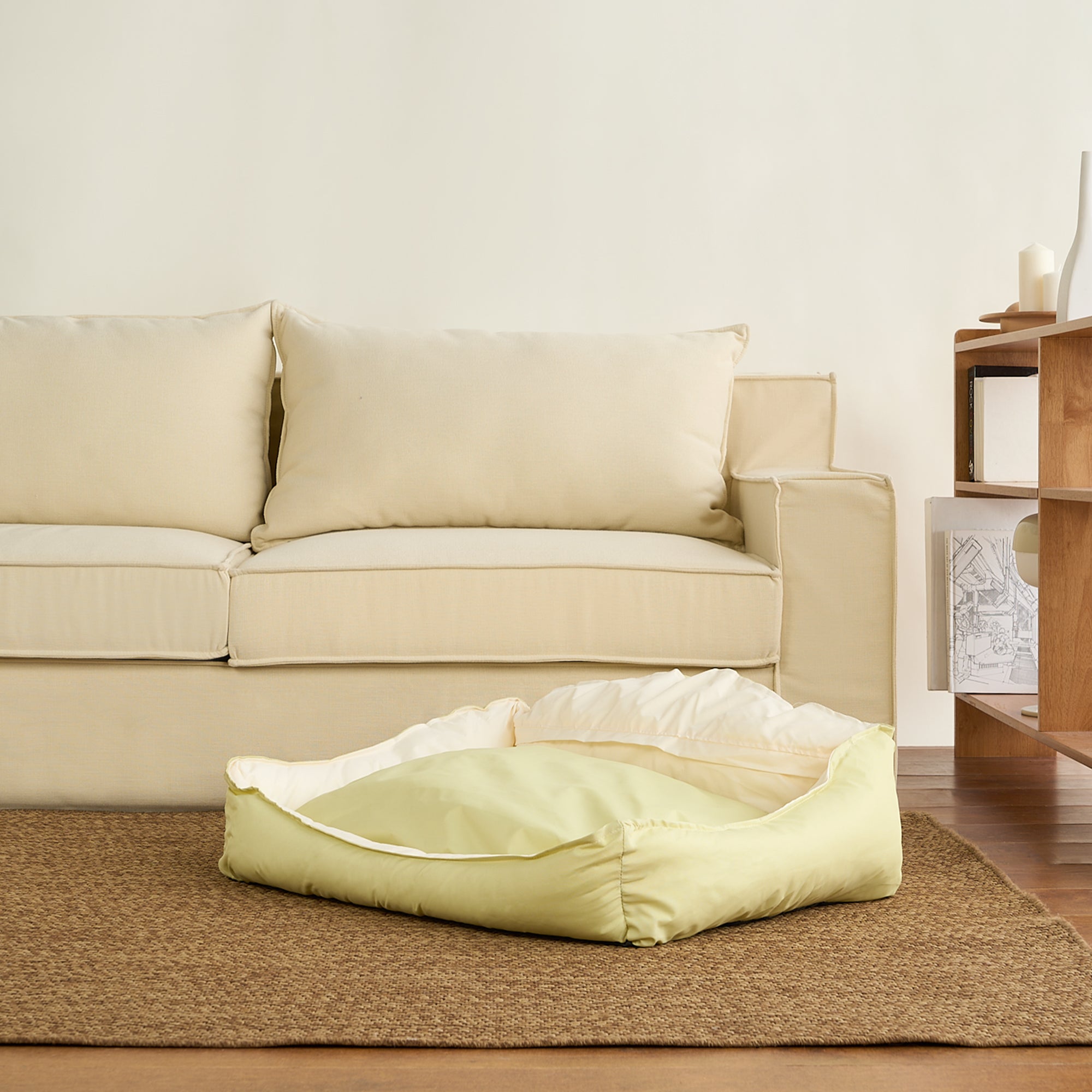 Gelbes Haustierbett aus Baumwolle auf Teppich vor beigem Sofa im Wohnzimmer.