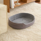 Graues Hundebett aus Stoff auf Teppich, oval, gemütlich, ideal für kleine Haustiere.