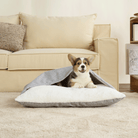 Corgi in grauem, ultraweichem Haustier-Schlafsack auf beigem Teppich vor Sofa.
