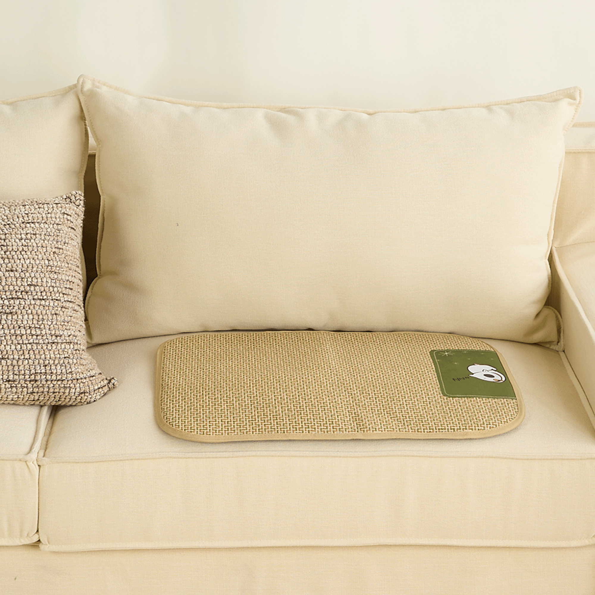 Geflochtete Rattan-Kühlmatte für Haustiere auf beigem Sofa, ideal für Sommerhitze.