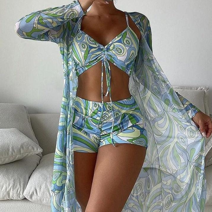Frau in stilvollem, gemustertem Sommeroutfit mit Crop-Top, Shorts und transparentem Überwurf. Perfekt für Strandmode und Freizeitkleidung.