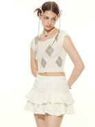 Junge Frau in weißem, kurzem Stricktop mit Rautenmuster und Rüschenrock. Modetrend, Sommeroutfit, stilvoll, feminin, lässig, elegant.