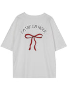 Weißes T-Shirt mit roter Schleife und "La Vie en Rose" Aufdruck. Modisches Damenoberteil, ideal für lässige Outfits. Hochwertige Baumwolle.