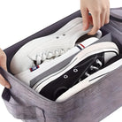 Person legt weiße und schwarze Sneaker in graue Aufbewahrungsbox, Schuhorganisation, platzsparend.