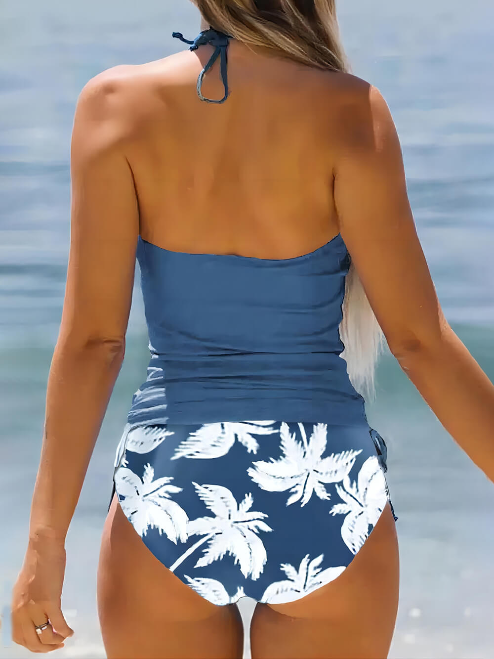 Frau im blauen Badeanzug mit Palmenmuster am Strand, Sommermode, Bademode, Urlaub.