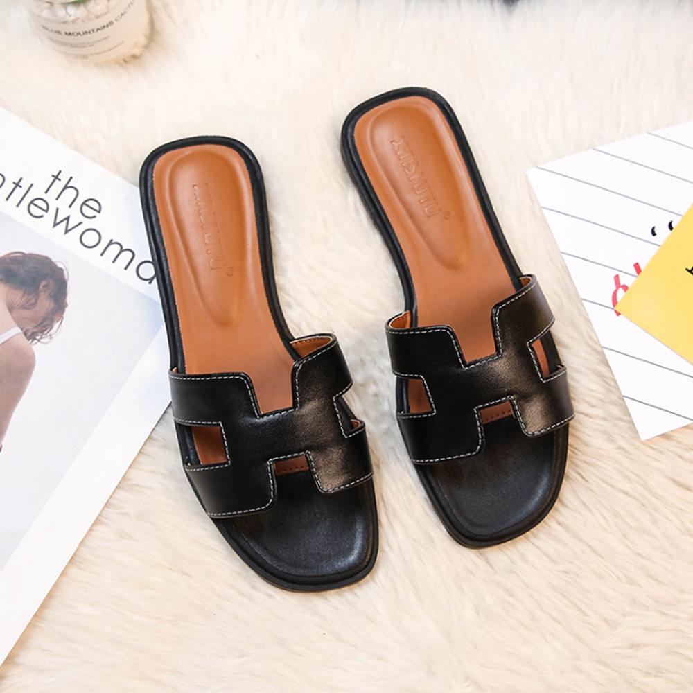 Schwarze Ledersandalen mit offenem Zehenbereich auf weißem Teppich. Modische Damen-Slipper, ideal für Sommer und Freizeit.