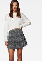 Damenmode: Weißer Pullover und grauer, gemusterter Rock mit Rüschen. Stilvoller Look für Herbst/Winter. Trendige Kleidung für Frauen.