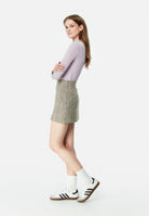 Frau in lila Pullover und karierter Minirock, weiße Socken, Adidas-Sneaker. Modetrend, lässiger Look, stilvolle Damenbekleidung.