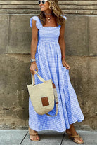 Frau in blau-weiß kariertem Maxikleid, trägt Strohtasche und Sonnenbrille. Sommermode, lässiger Stil, trendiges Outfit, Stadtbummel.