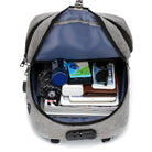 Grauer Rucksack mit Laptopfach, geöffnet, gefüllt mit Elektronik und Zubehör, Diebstahlschutz.