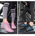 Zwei Paar Barfußschuhe auf Laufband: Rosa Damenmodell und schwarzes Herrenmodell. Ideal für Fitness, Laufen und Sport. Leicht und atmungsaktiv.