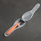 Rasierer mit orangefarbenem Griff in transparenter Kunststoffhülle auf grauem Hintergrund.