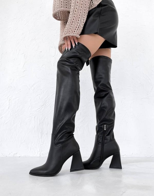 Damen Overknee-Stiefel aus schwarzem Leder mit Blockabsatz, kombiniert mit kurzem Rock und Strickpullover. Trendige Herbstmode 2023.