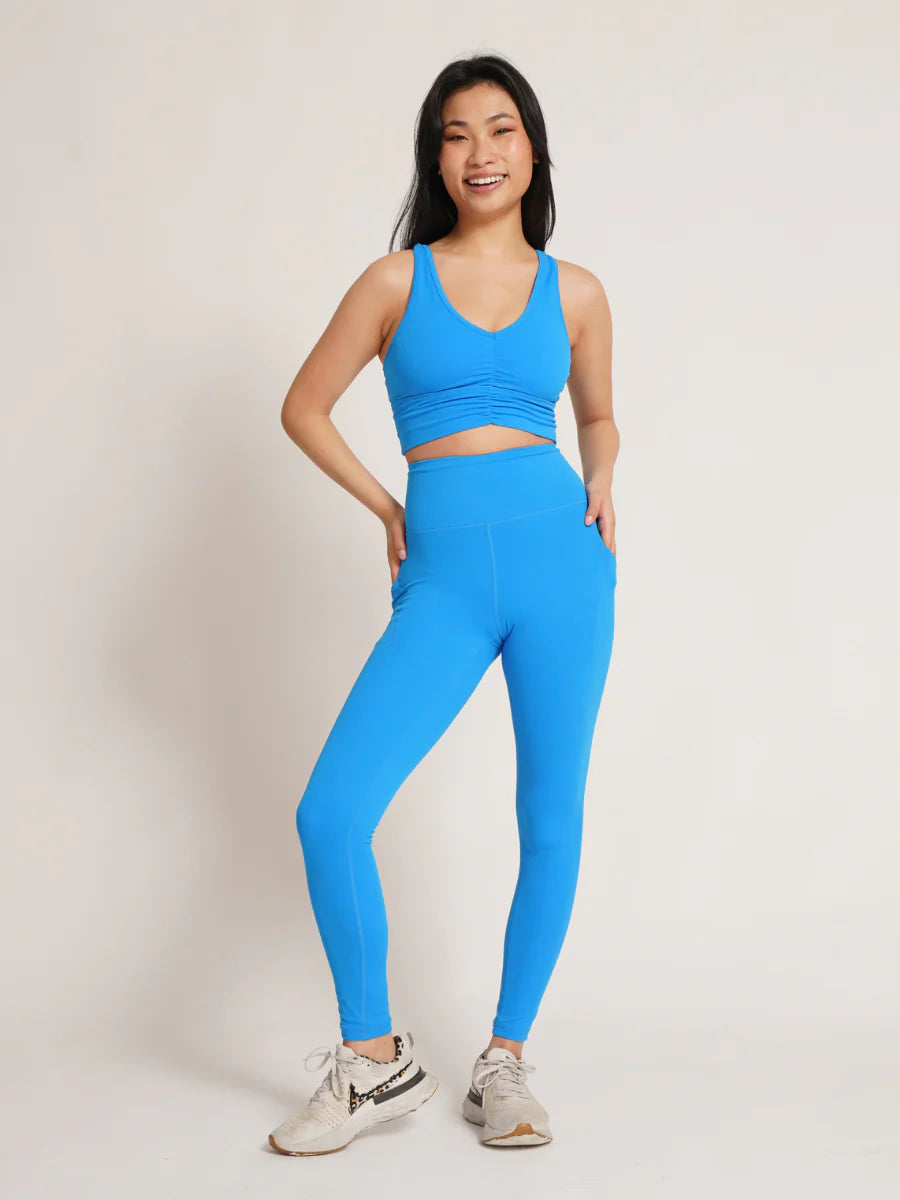 Frau in blauer Sportbekleidung, bestehend aus Leggings und Top, lächelt. Perfekt für Yoga, Fitness und aktive Freizeit. Bequeme, stilvolle Sportmode.