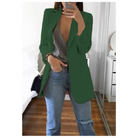Frau in grünem Blazer, grauem Top und blauen Jeans posiert im modernen Schlafzimmer. Trendige Damenmode, stilvolle Freizeitkleidung.