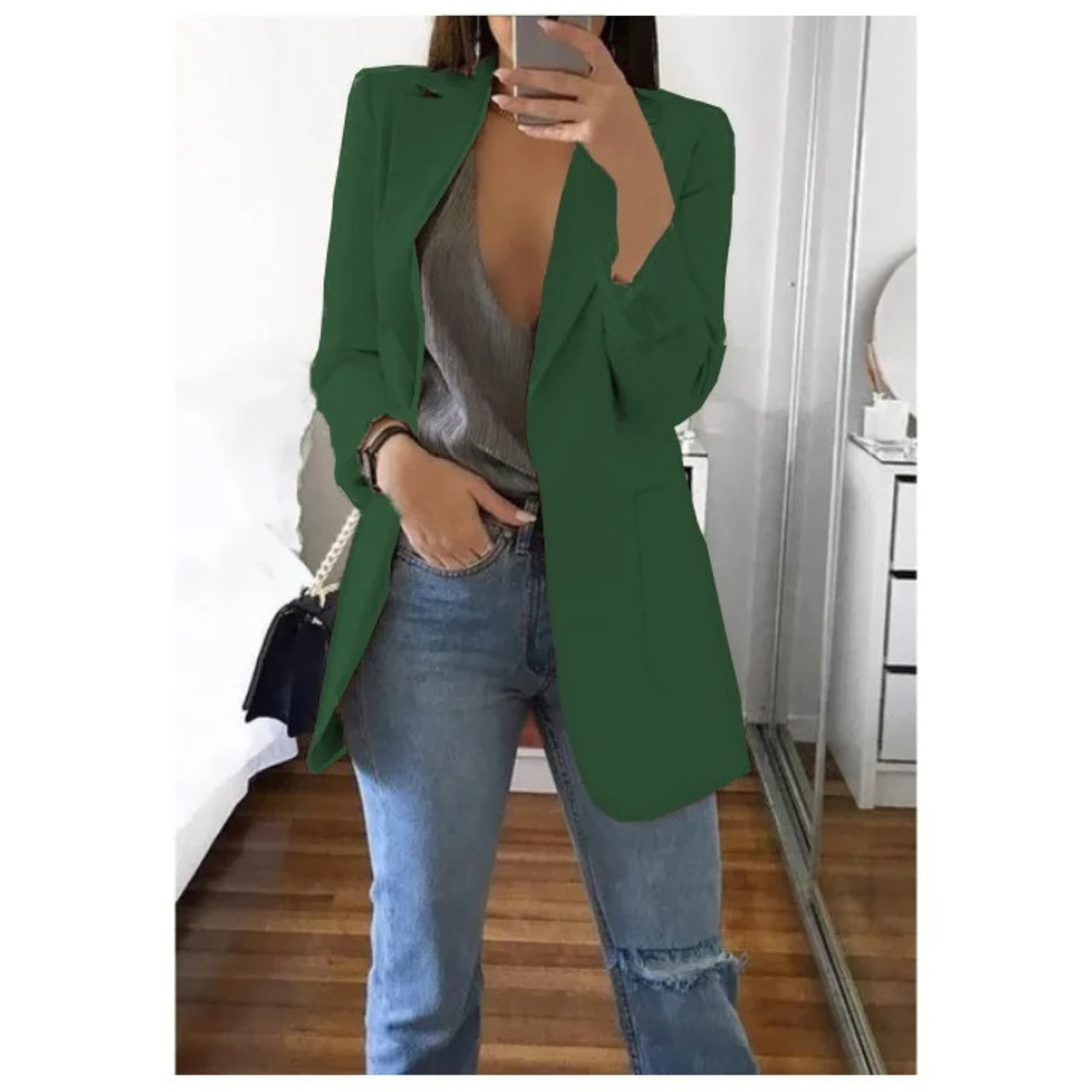 Frau in grünem Blazer, grauem Top und blauen Jeans posiert im modernen Schlafzimmer. Trendige Damenmode, stilvolle Freizeitkleidung.