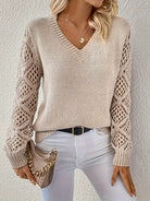 Beiger Strickpullover mit V-Ausschnitt und gehäkelten Ärmeln, kombiniert mit weißer Hose und modischer Handtasche. Perfekt für Damenmode im Herbst.