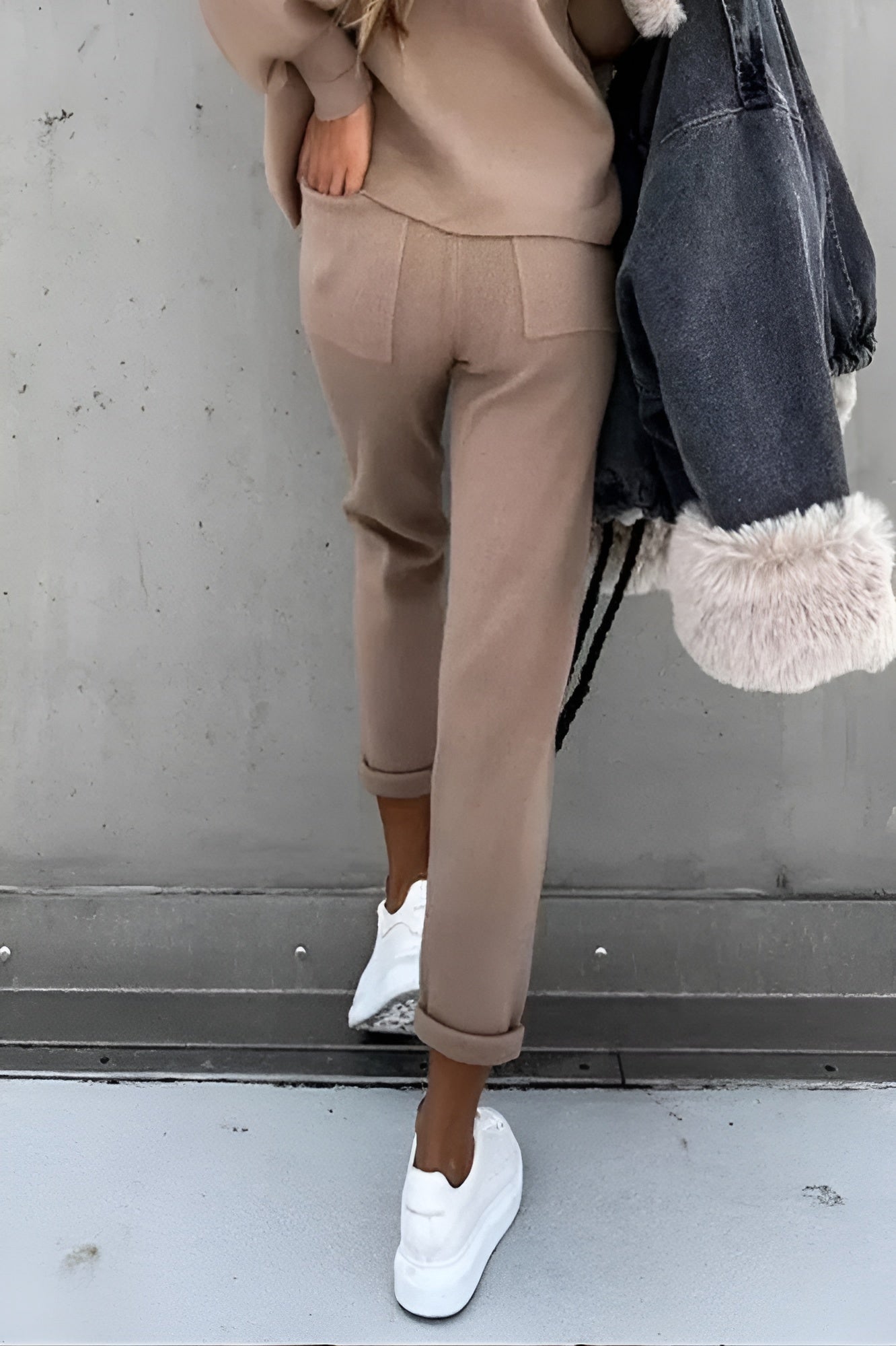 Damenmode: Beige Jogginghose, lässig geschnitten, kombiniert mit weißen Sneakern und einer grauen Jacke mit Fellbesatz. Trendige Freizeitkleidung.