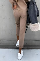 Damenmode: Beige Jogginghose, lässig geschnitten, kombiniert mit weißen Sneakern und einer grauen Jacke mit Fellbesatz. Trendige Freizeitkleidung.