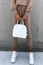 Elegante Frau in beiger Kleidung mit weißer Handtasche und Sneakers. Modetrend, Streetstyle, Damenmode, Accessoires, urbaner Look.