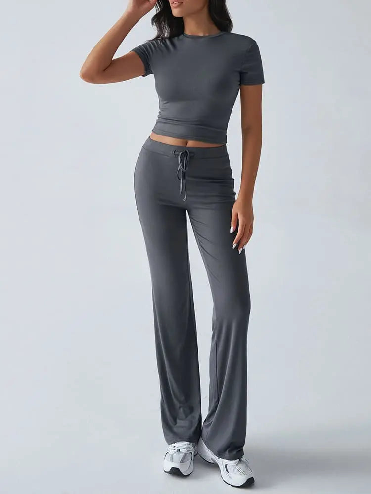 Damen-Sportanzug in Grau, bestehend aus kurzärmeligem Crop-Top und weiten Hosen. Ideal für Fitness, Yoga und Freizeit. Bequem und stilvoll.