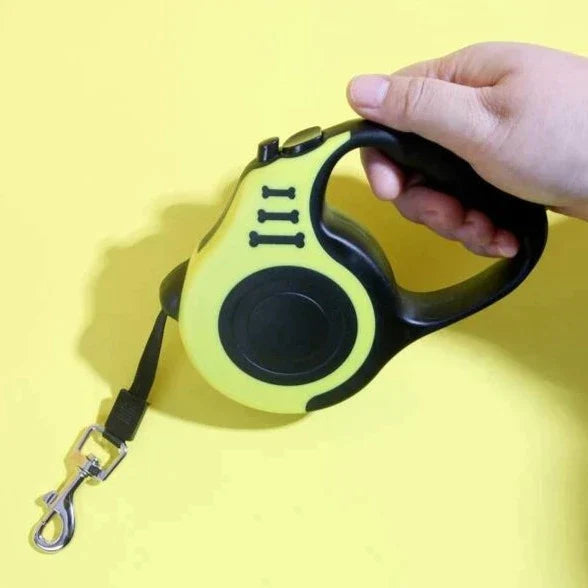 Hand hält gelbe Hundeleine mit automatischer Aufrollfunktion, schwarzem Griff und Metallhaken.