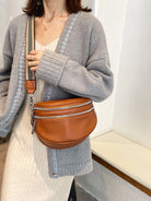 Damenmode: Elegante braune Leder-Gürteltasche mit silbernen Reißverschlüssen, kombiniert mit grauem Cardigan und gestreiftem Schulterriemen.