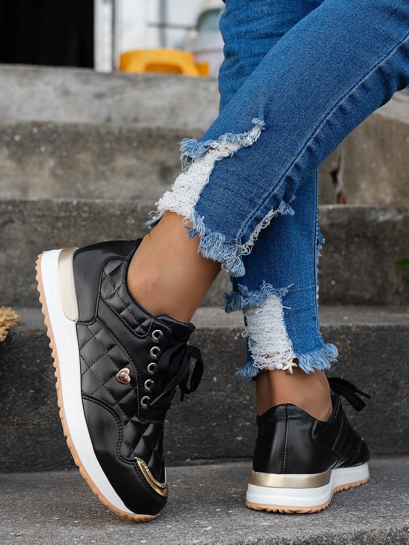Schwarze Damen-Sneaker mit Steppdesign, goldenen Akzenten und weißer Sohle, kombiniert mit zerrissenen Jeans. Perfekt für modische Freizeitlooks.