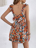 Frau in geblümtem Sommerkleid mit Rückenausschnitt und Schleife, orange-blaues Muster.