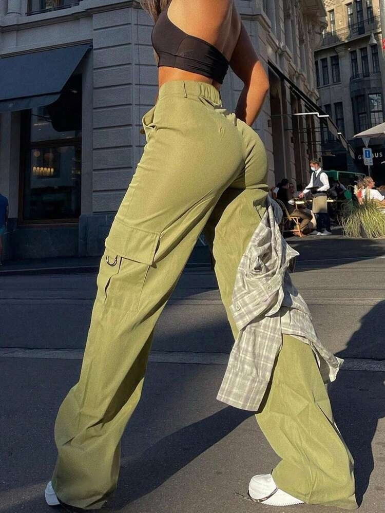 Frau in grüner Cargohose und schwarzem Top auf städtischer Straße. Modetrend, Streetwear, lässiger Stil, urbane Mode, Sommeroutfit.