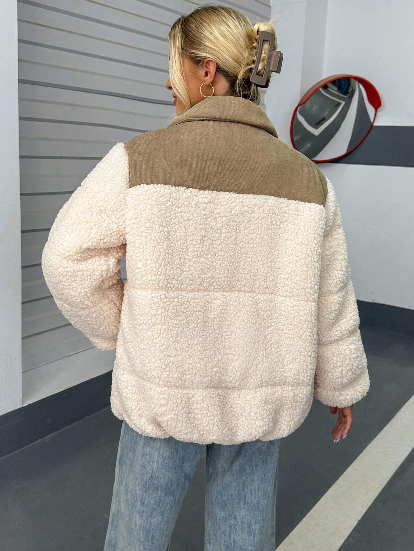 Frau trägt modische Teddyjacke in Cremeweiß, kombiniert mit blauer Jeans. Wintermode, kuscheliger Look, trendige Damenbekleidung.