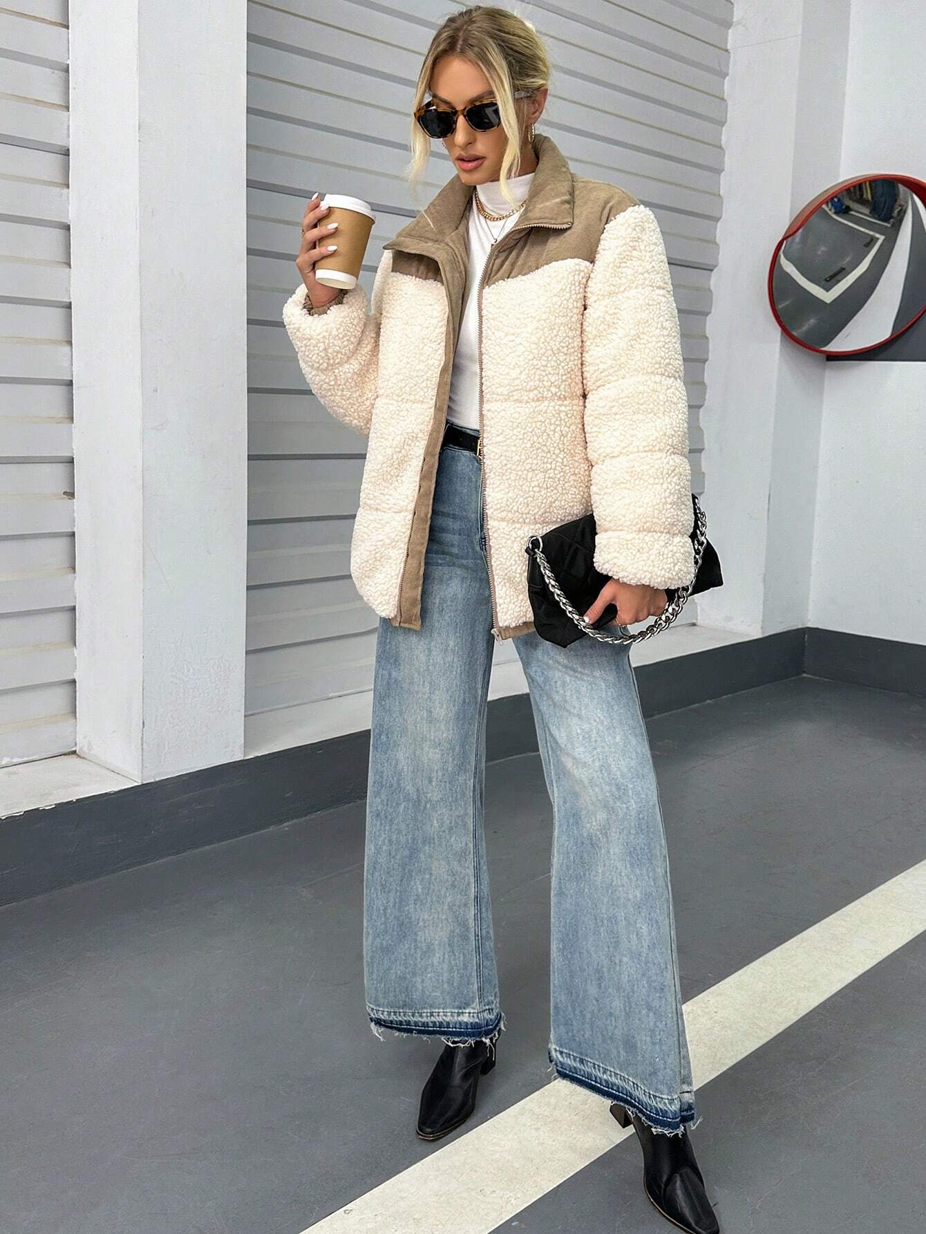 Frau in modischer Teddyjacke, weiten Jeans und schwarzen Stiefeletten, hält Kaffeebecher. Trendige Wintermode, Streetstyle, Damenbekleidung.