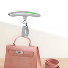 Digitale Kofferwaage mit Haken, silber, über rosa Handtasche, tragbar, präzise Gewichtsmessung.