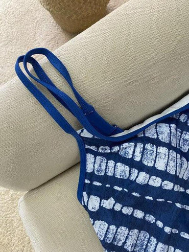 Blau-weißes Batik-Kleid mit Spaghettiträgern auf beigem Sofa. Sommermode, trendiges Design, lässiger Stil, ideal für warme Tage.