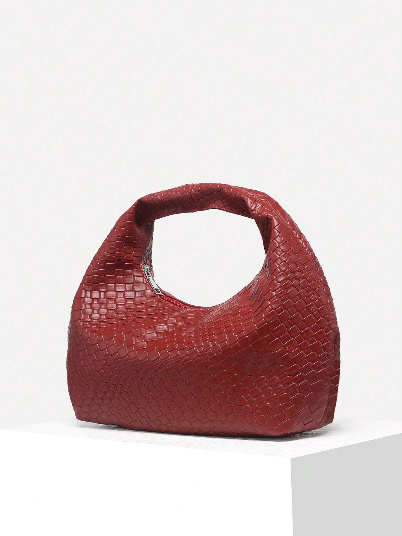 Rote Damenhandtasche aus Leder mit geflochtenem Muster auf weißem Podest.